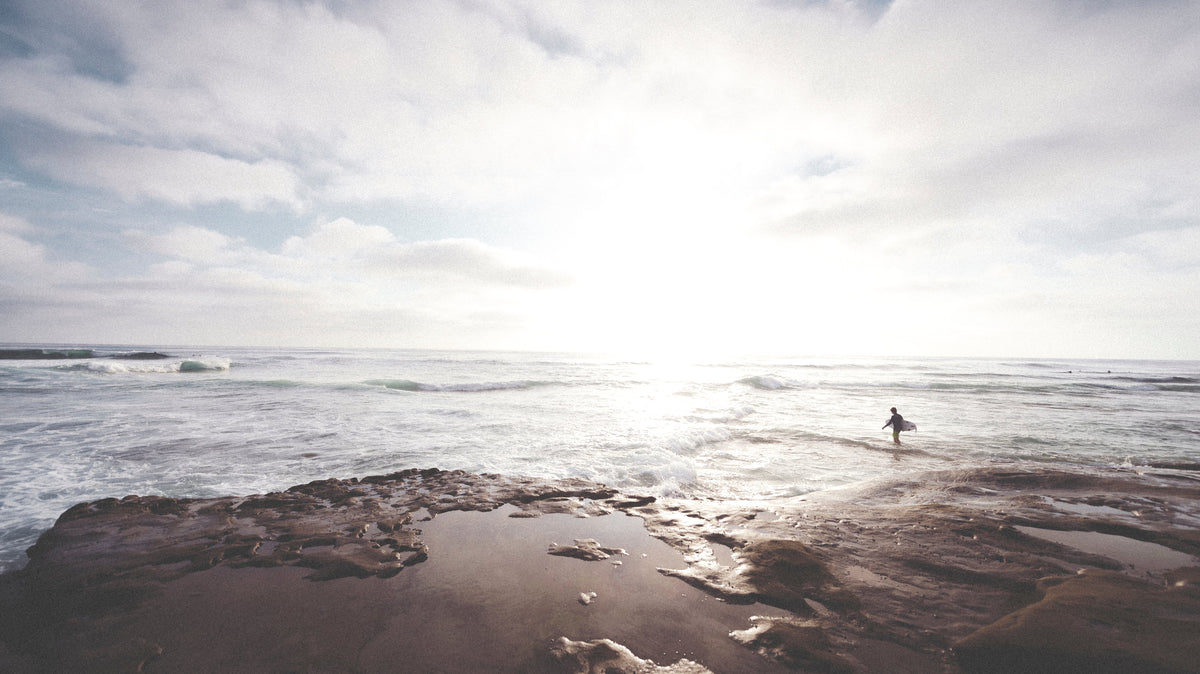 Surfista entrando al océano con su tabla al atardecer