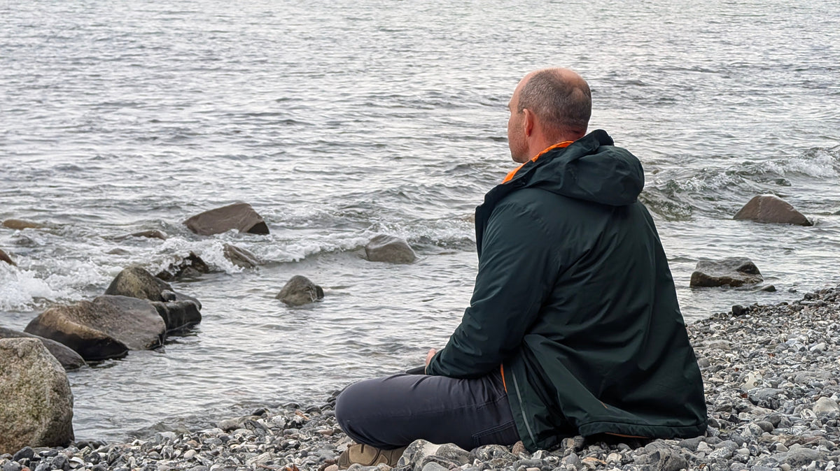 Hombre con chaqueta outdoor sentado frente al mar en otoño