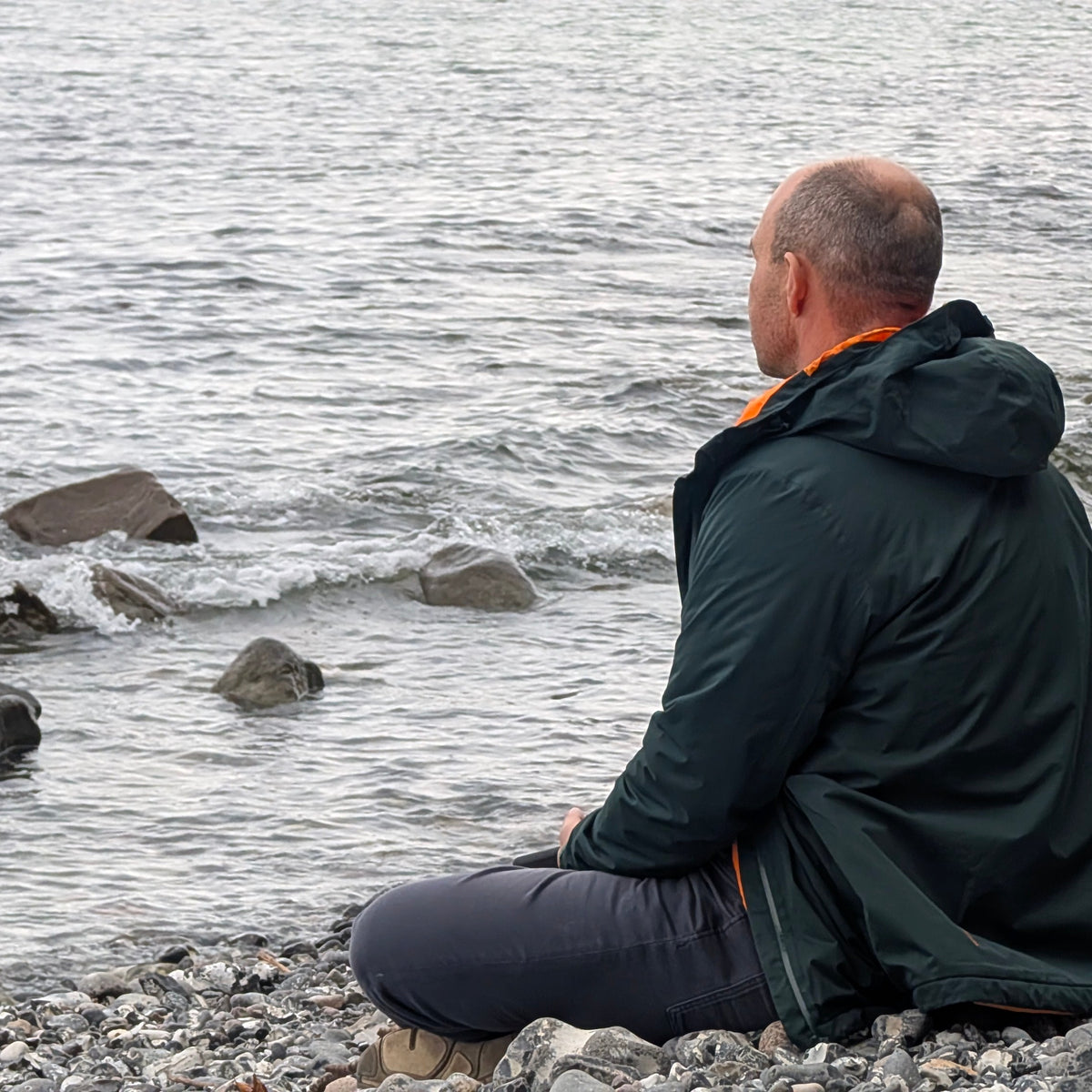 Hombre con chaqueta outdoor sentado frente al mar en otoño