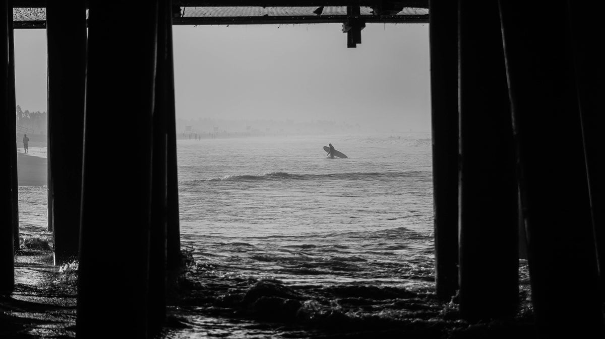 Surfista con tabla entre pilares junto al mar, portada real sobre cera de surf