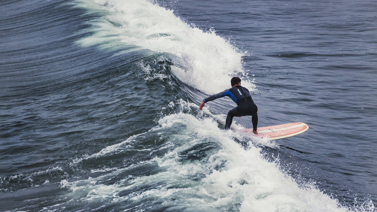 Surfista con traje de neopreno negro recorriendo una ola en Pismo Beach