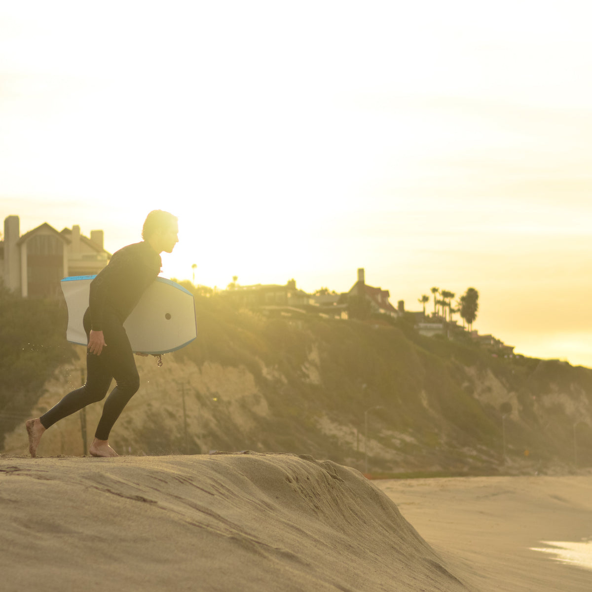 Surfista con traje de neopreno caminando al atardecer junto al mar