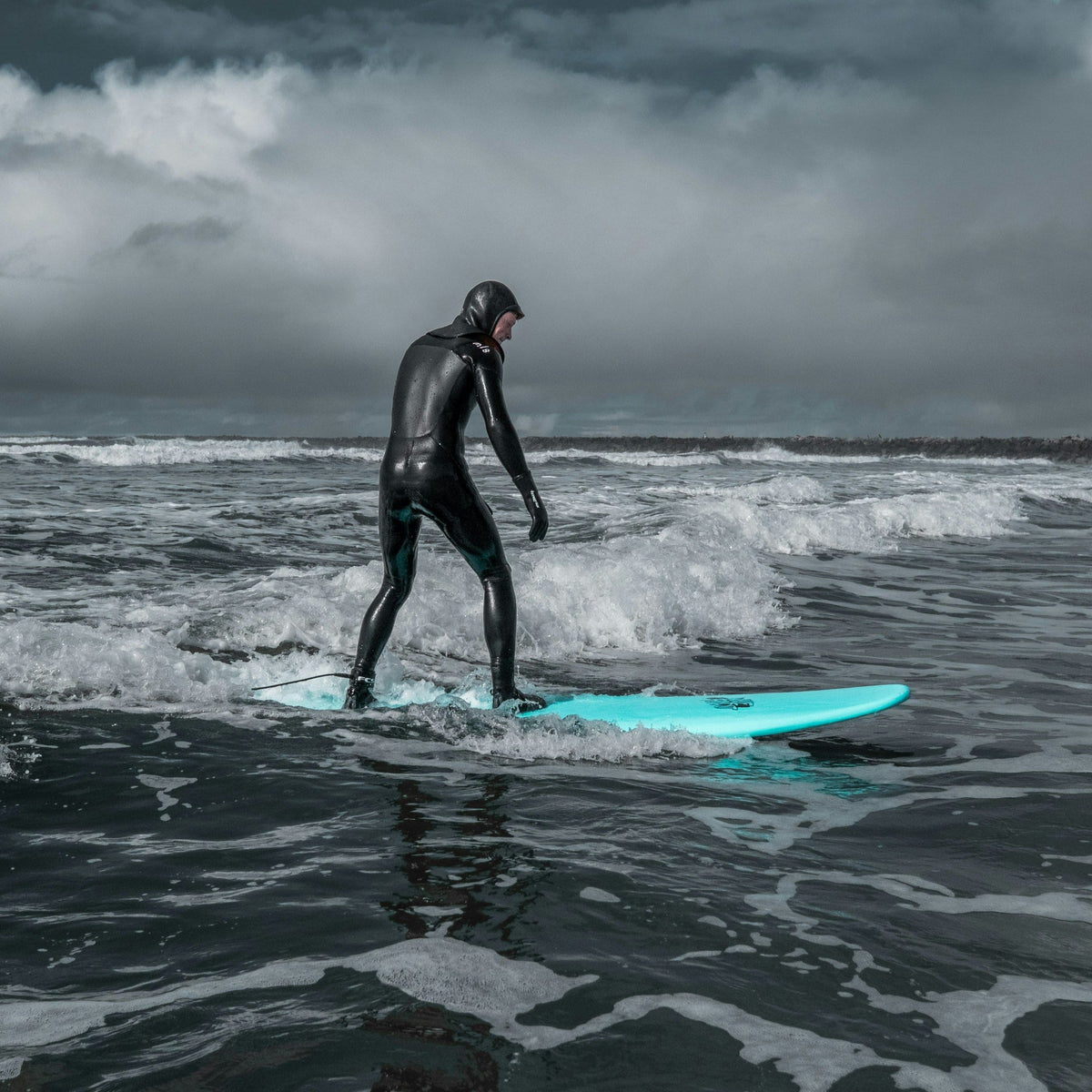Surfista con traje integral en una sesión de agua fría bajo cielo cubierto