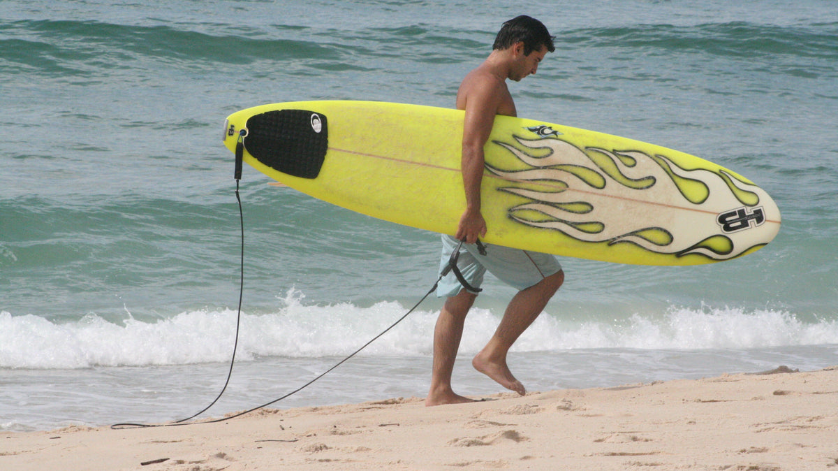 Surfista caminando por la playa con una tabla equipada con leash