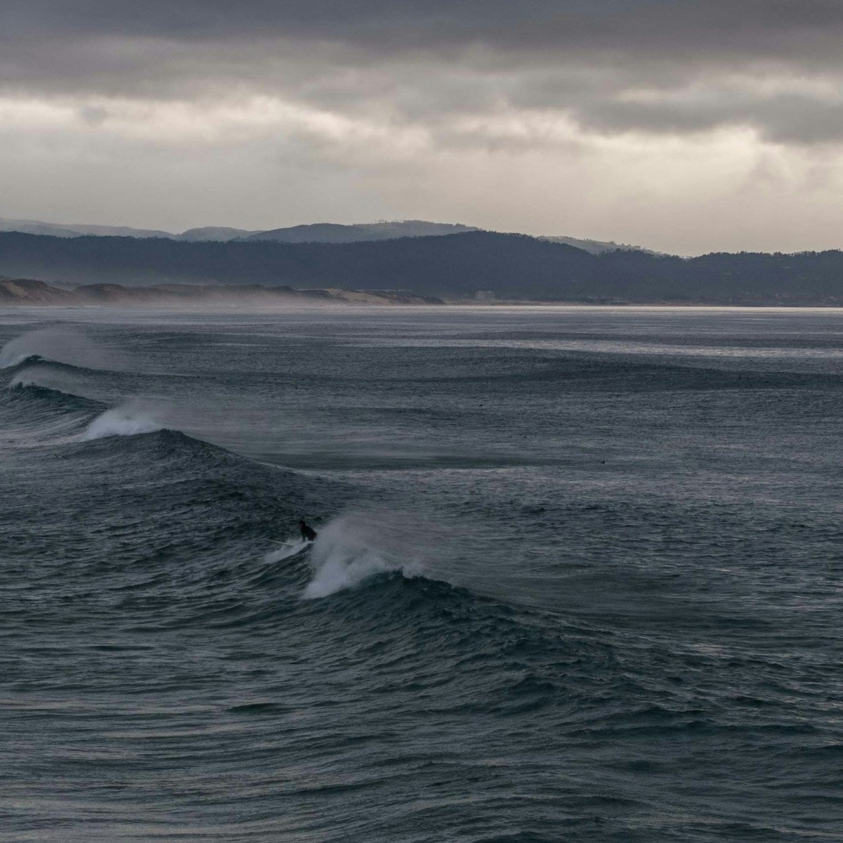 Surfista frente a olas bajo un cielo cubierto