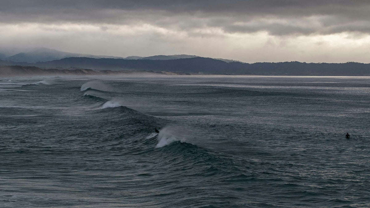 Surfista frente a olas bajo un cielo cubierto