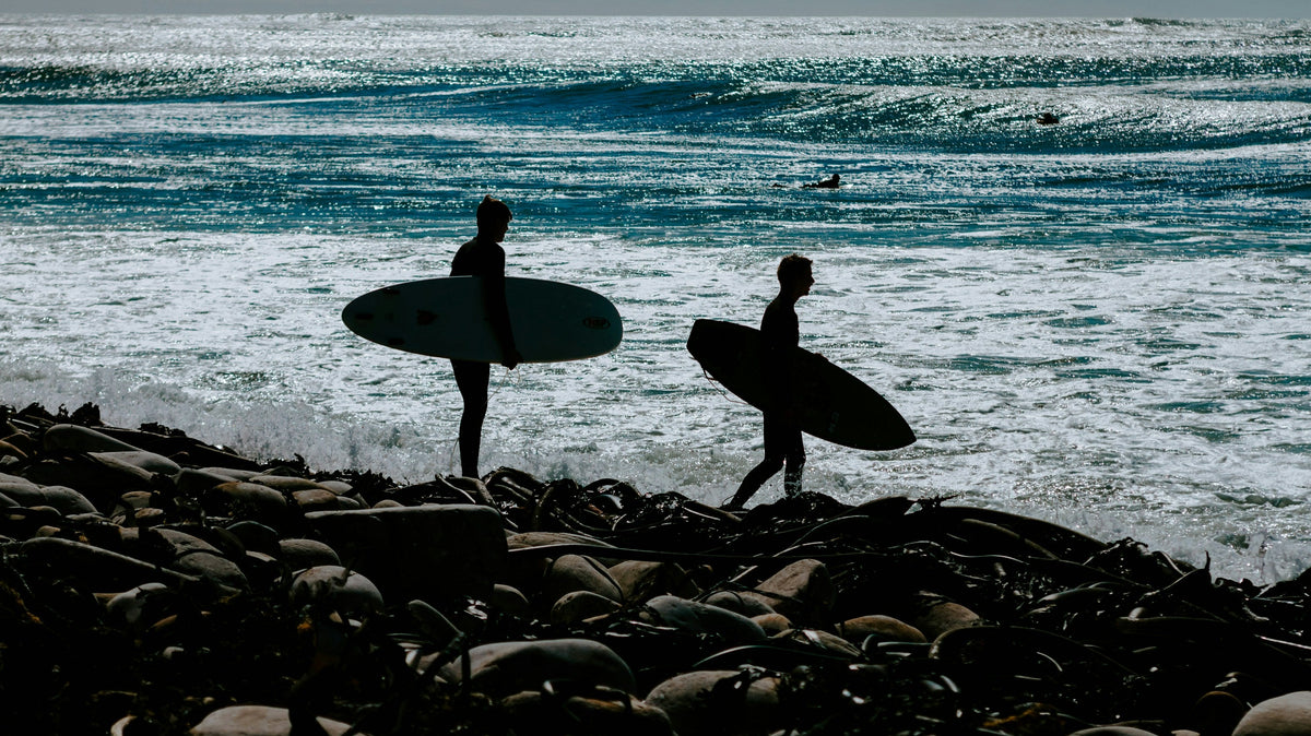Dos surfistas caminando por una costa rocosa con sus tablas