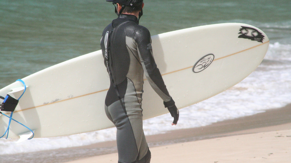 Surfista caminando hacia el mar con tabla y neopreno antes de una sesión; imagen real usada en THE SURF TOWN JOURNAL. Foto: Johntex / Wikimedia Commons, CC BY 2.5.