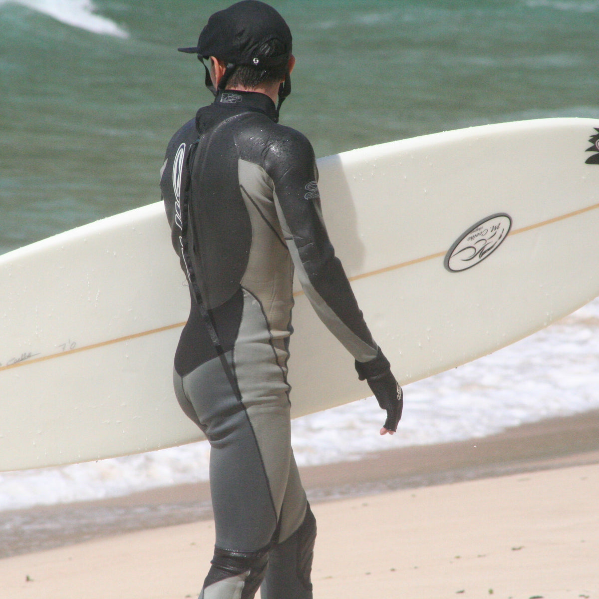 Surfista caminando hacia el mar con tabla y neopreno antes de una sesión; imagen real usada en THE SURF TOWN JOURNAL. Foto: Johntex / Wikimedia Commons, CC BY 2.5.