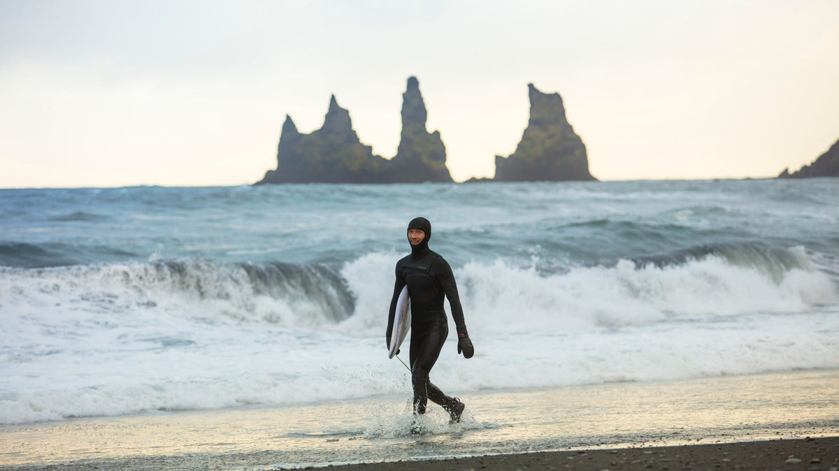 Surfista caminando con su tabla sobre una playa de arena negra