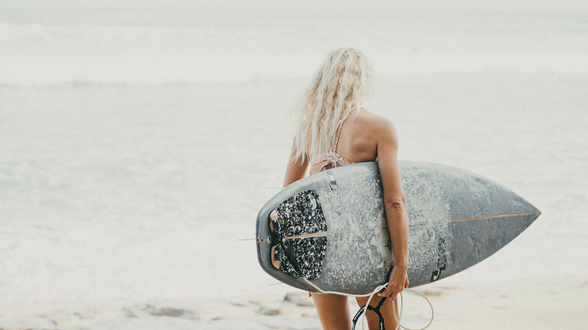 Surfista de espaldas caminando hacia el mar con su tabla de surf