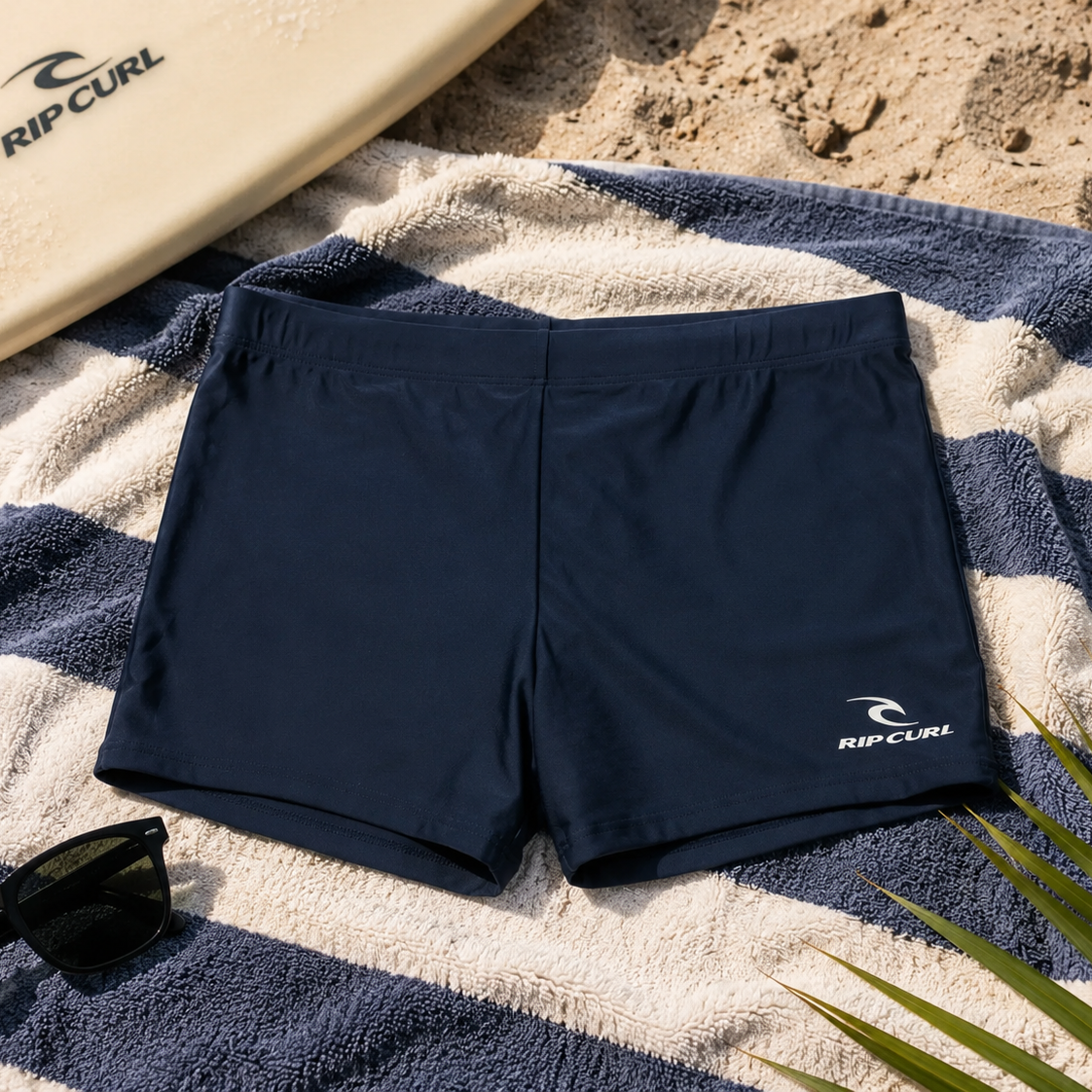 Bañador de natación Rip Curl Corp Boyleg Sluggo Dark Navy sobre toalla de playa en escena surf lifestyle premium