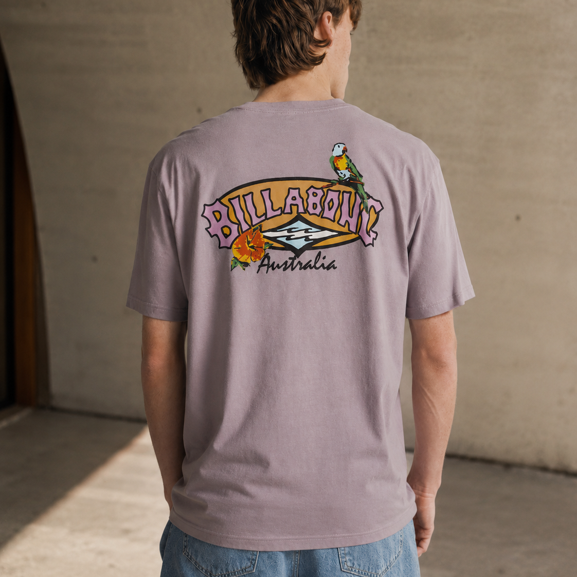 Camiseta Billabong Origin Purple Ash para hombre con estampado tropical trasero en escena editorial surf premium de estilo minimalista y luz cálida natural.
