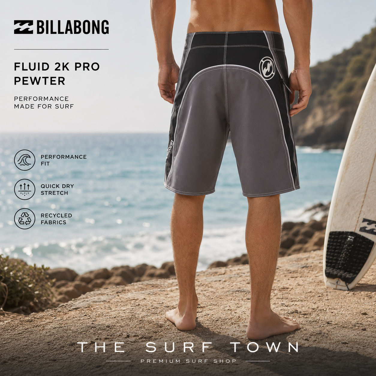Bañador Billabong Fluid 2K Pro Pewter de 21 pulgadas para hombre, fotografía editorial propia de THE SURF TOWN en un entorno costero junto al mar y una tabla de surf, con corte largo que cae hasta media rodilla y diseñado para surf de alto rendimiento y estilo de vida beach lifestyle.