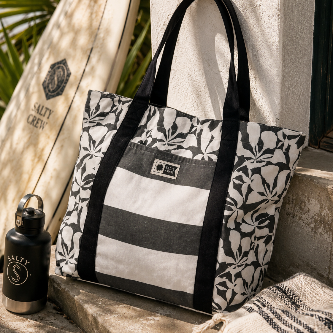 Bolso de playa Salty Crew Ashor Beach Bag Black para mujer en escena lifestyle surf junto a tabla de surf y accesorios premium de playa