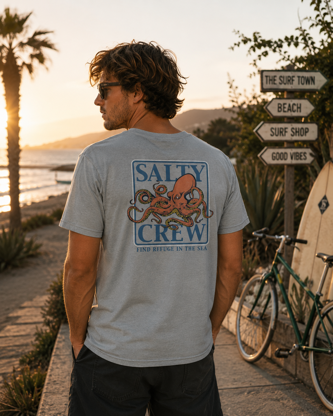 Camiseta hombre Salty Crew pulpo Ink Slinger Tee color quarry en paseo marítimo surf lifestyle premium con cartel The Surf Town al atardecer Costa del Sol