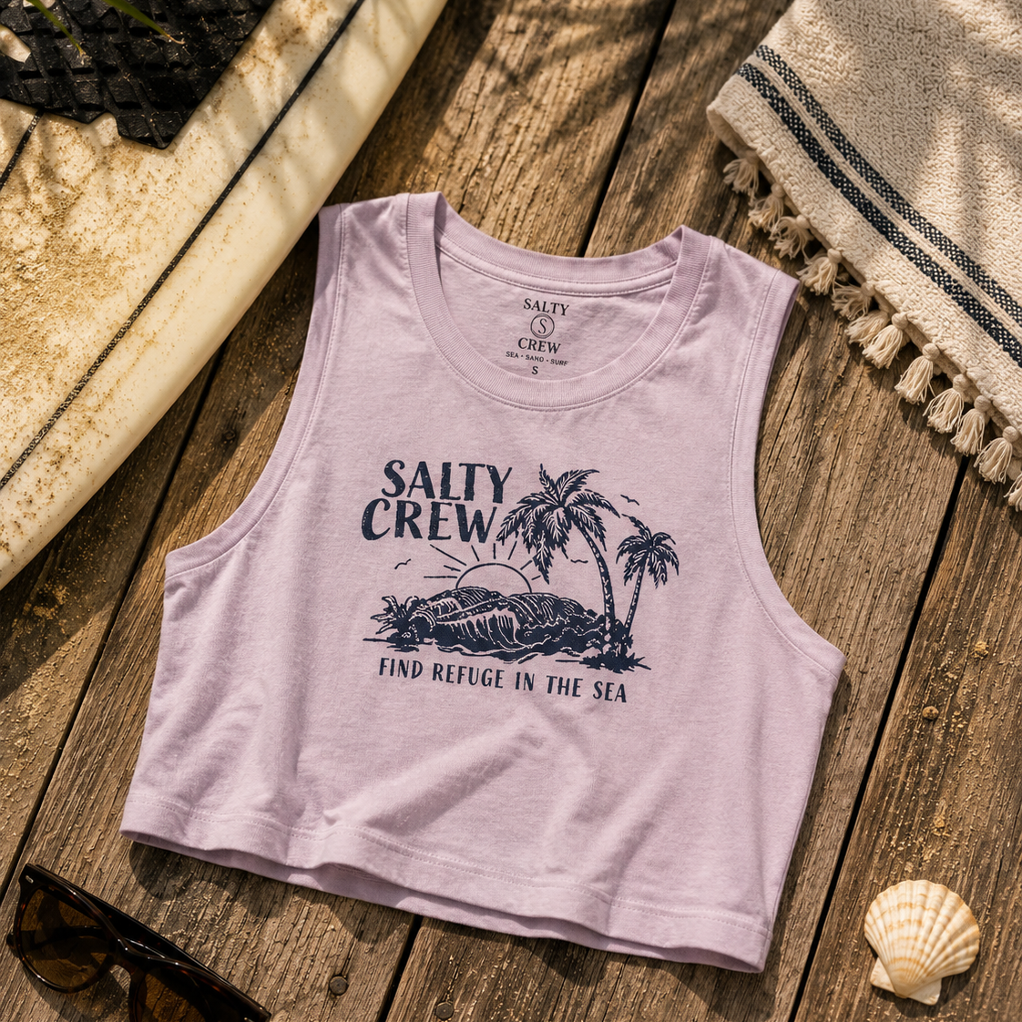 Camiseta cropped Salty Crew Outside Tank Pale Orchid para mujer sobre fondo lifestyle de playa con tabla de surf y accesorios surferos premium
