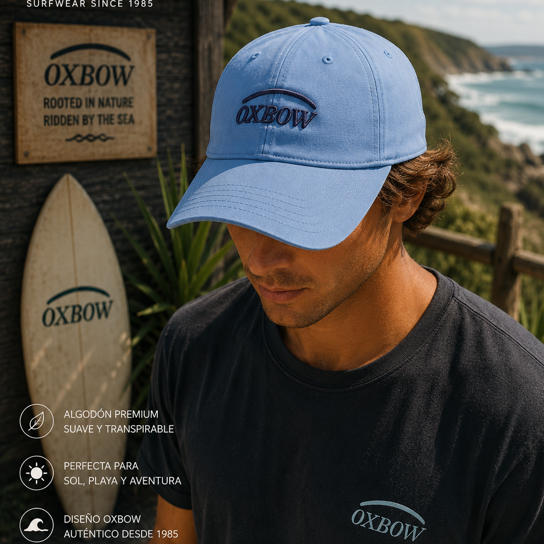 Gorra Oxbow Elini Lost Blue azul con logo frontal en escenario coastal premium y estética editorial surf cinematográfica