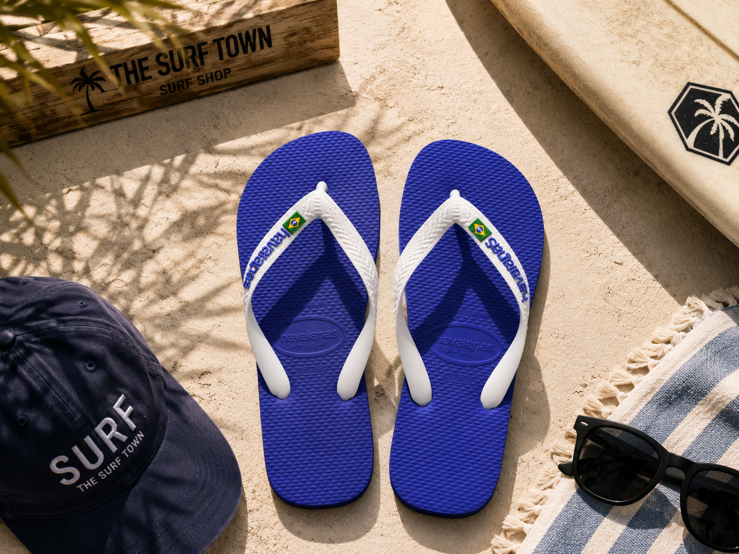 Chanclas Havaianas Brasil Logo azul naval sobre arena mediterránea junto a accesorios surf premium y detalle The Surf Town Surf Shop