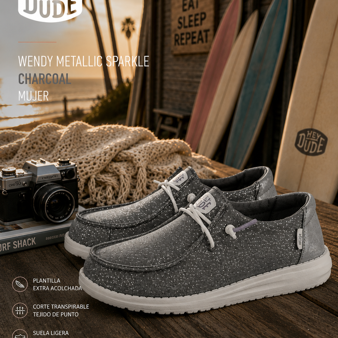 Zapatillas Hey Dude Wendy Metallic Sparkle Charcoal para mujer en escenario surf lifestyle premium con estética coastal cinema y luz dorada editorial