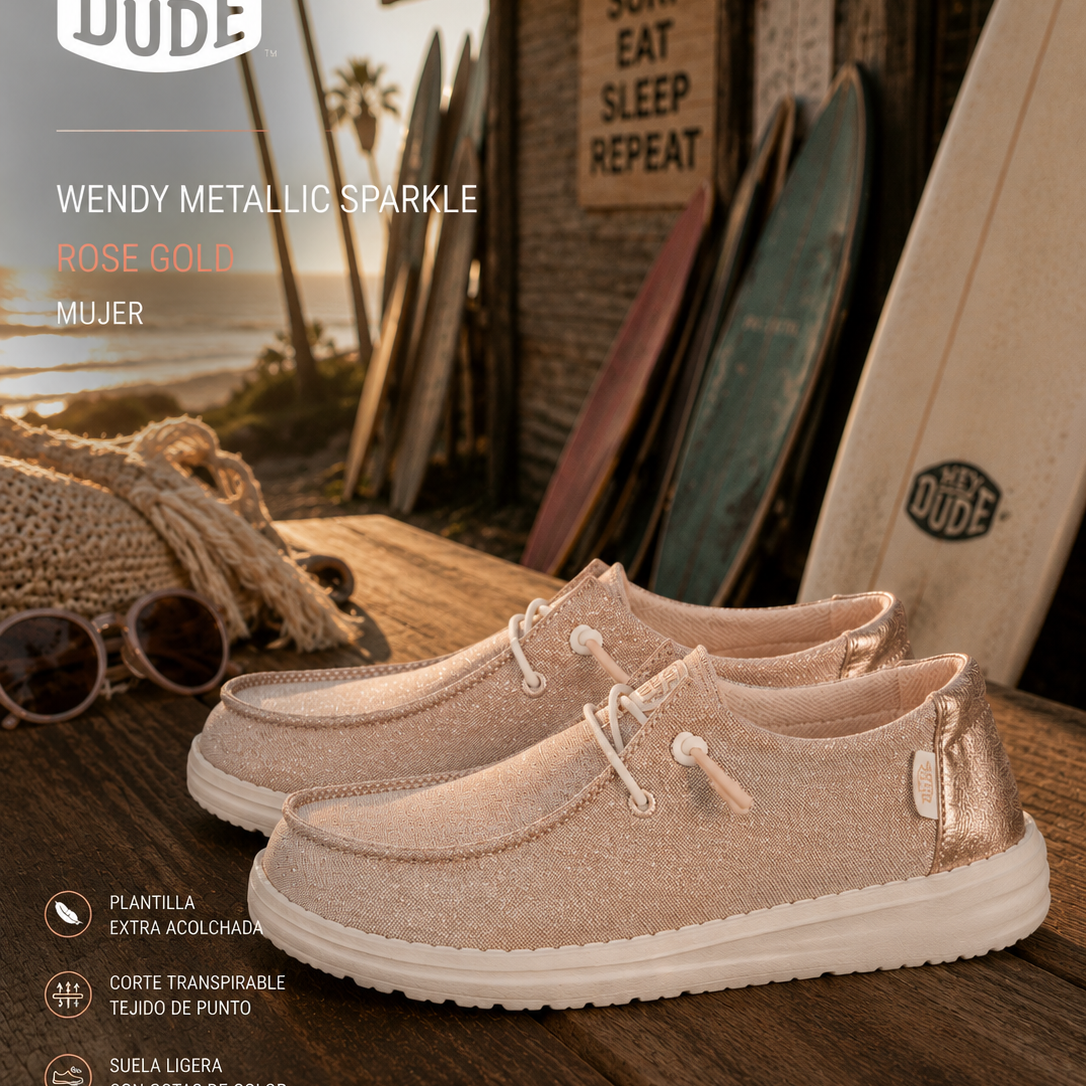 Zapatillas Hey Dude Wendy Metallic Sparkle Rose Gold para mujer en escenario surf lifestyle premium con estética coastal cinema y luz dorada editorial