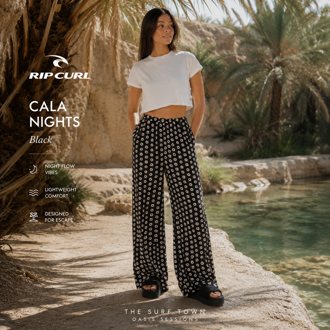 Fotografía propia de THE SURF TOWN de los pantalones Rip Curl Cala Nights Black para mujer en un oasis del desierto con agua cristalina, palmeras naturales y ambiente surf lifestyle premium.