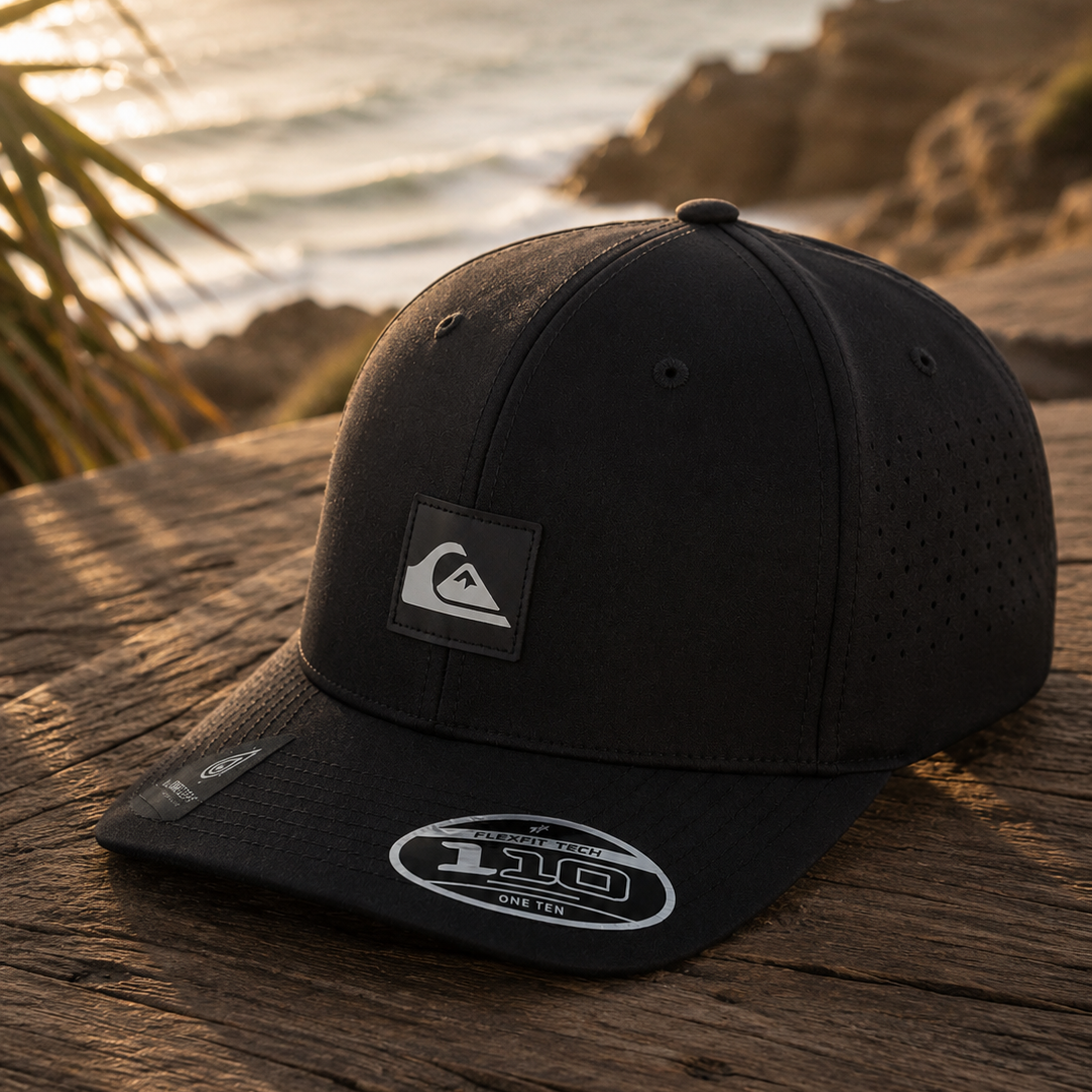 Gorra Quiksilver Adapted Black Flexfit Tech hombre estilo surf premium junto al mar al atardecer