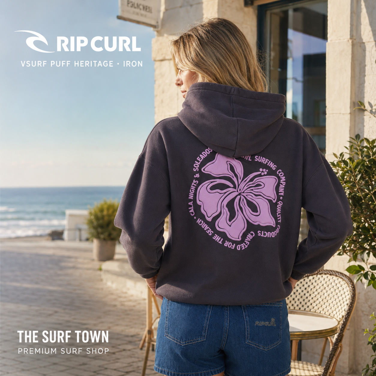 Sudadera de mujer Rip Curl Surf Puff Heritage Iron con capucha y estampado floral rosa, en una imagen editorial propia de THE SURF TOWN frente al mar.