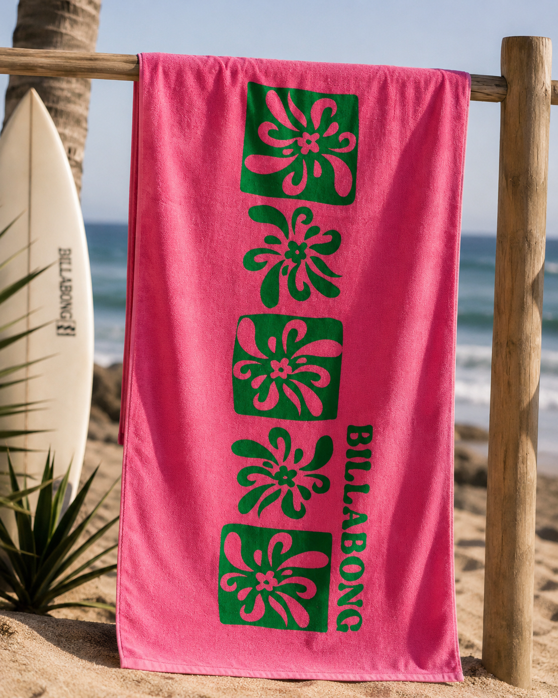 Toalla Billabong rosa y verde estilo surf lifestyle colgada en playa tropical junto al mar