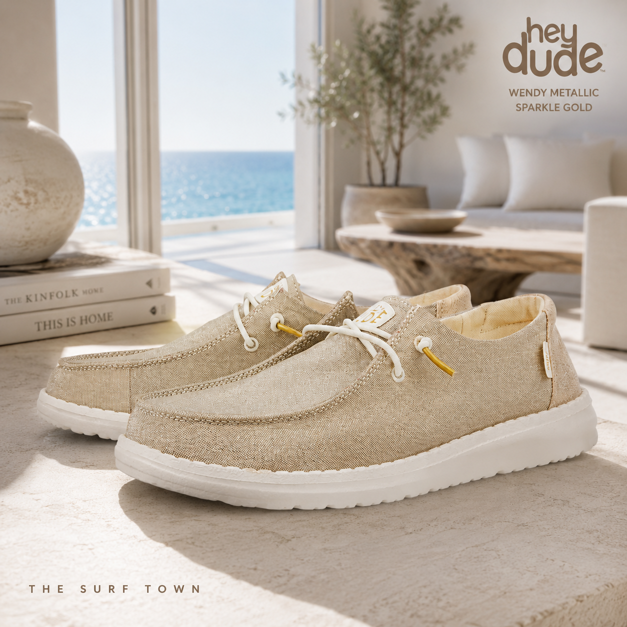Zapatillas Hey Dude Wendy Metallic Sparkle Gold en interior arquitectónico costero premium, imagen exclusiva creada por THE SURF TOWN con fotografía lifestyle elegante y luminosa