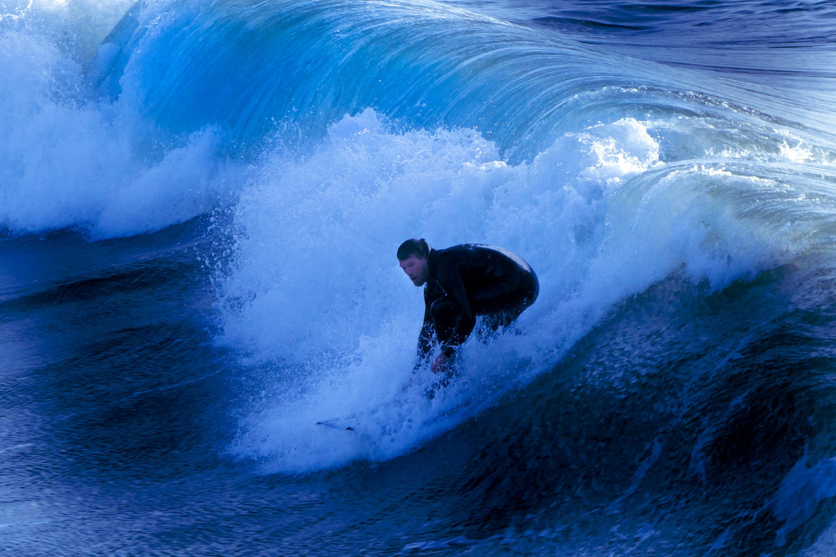 Surfista con traje de neopreno sobre una ola azul en un día frío de invierno