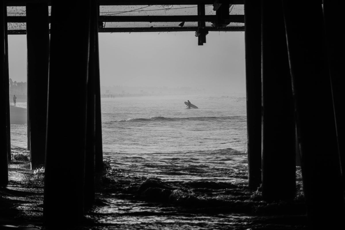 Surfista con tabla entre pilares junto al mar, portada real sobre cera de surf