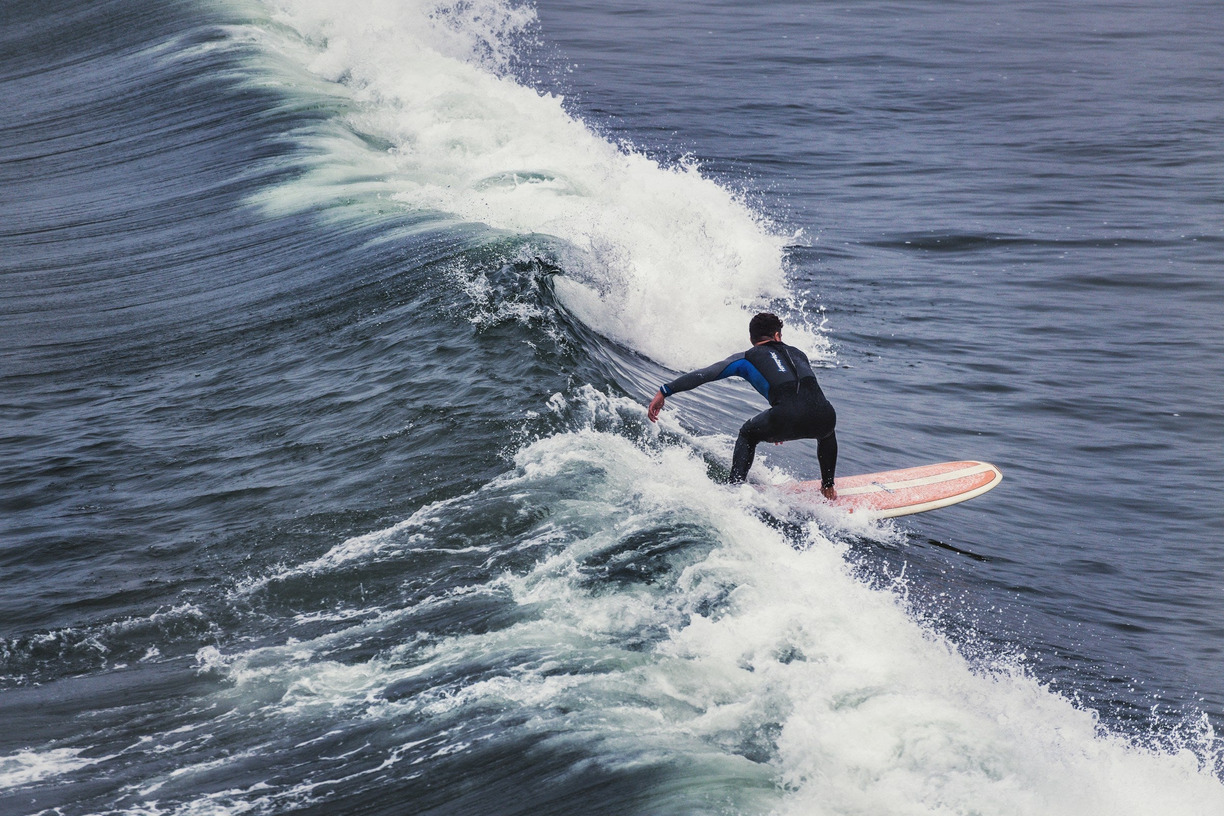 Surfista con traje de neopreno negro recorriendo una ola en Pismo Beach