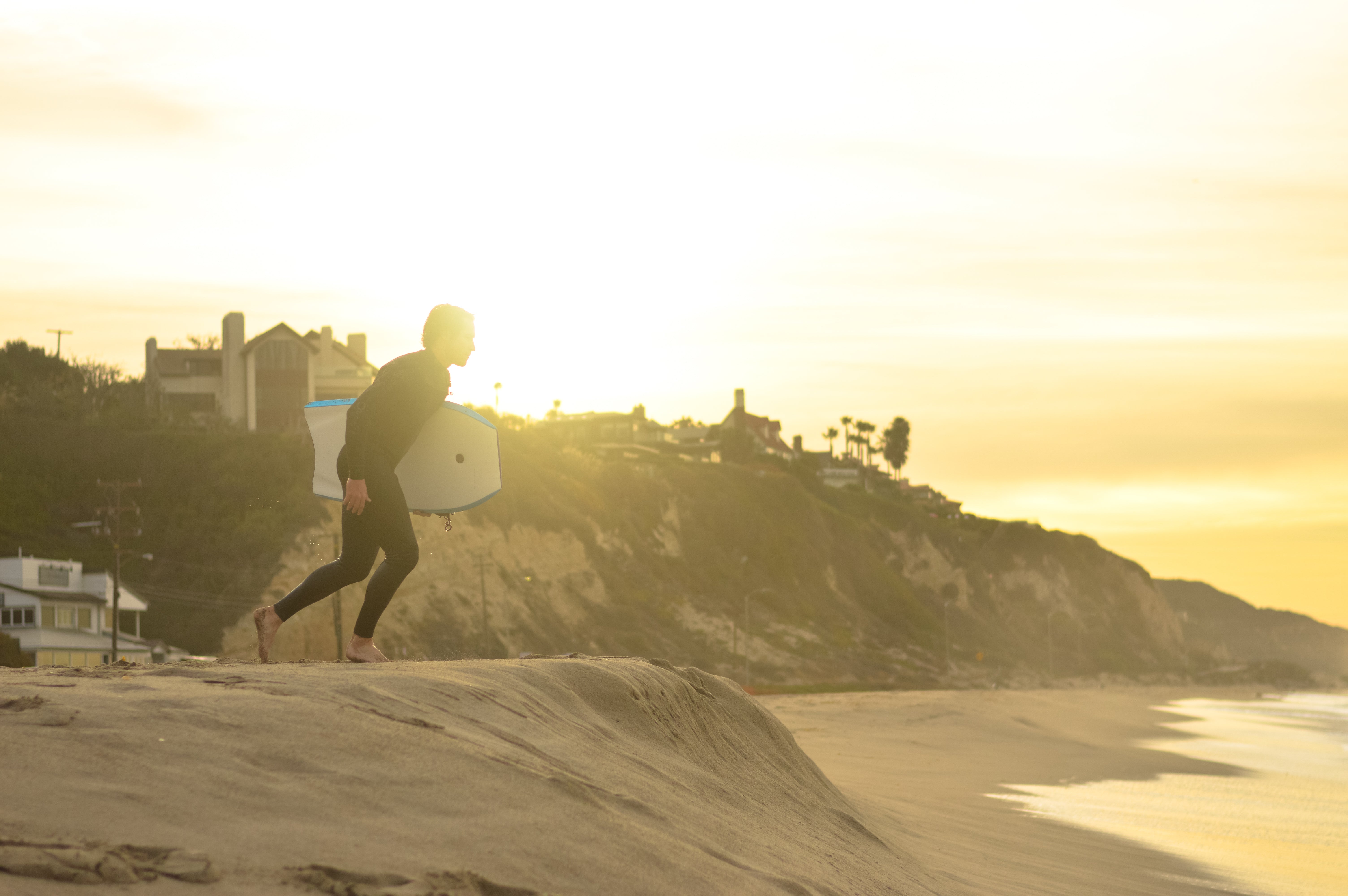 Surfista con traje de neopreno caminando al atardecer junto al mar