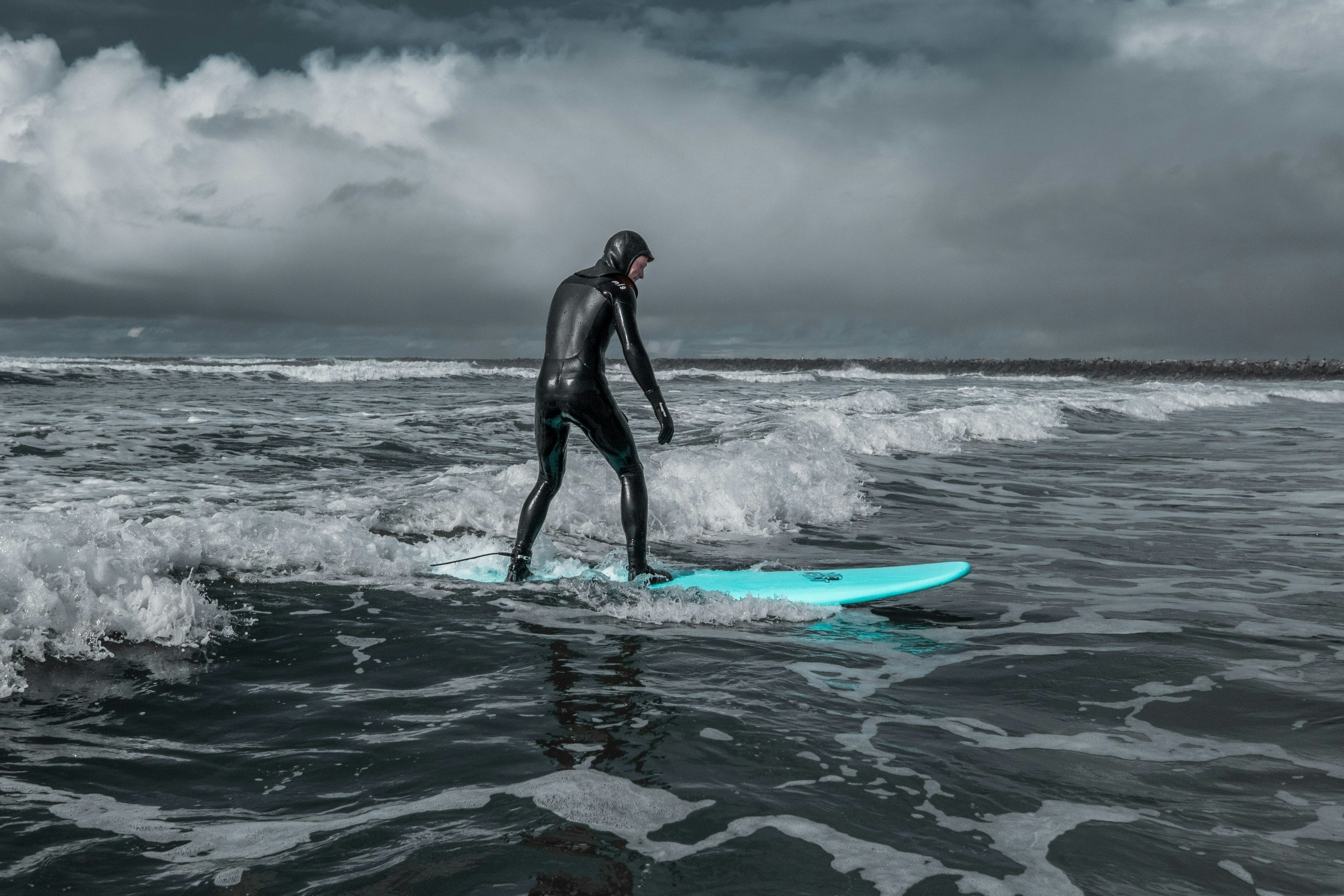 Surfista con traje integral en una sesión de agua fría bajo cielo cubierto