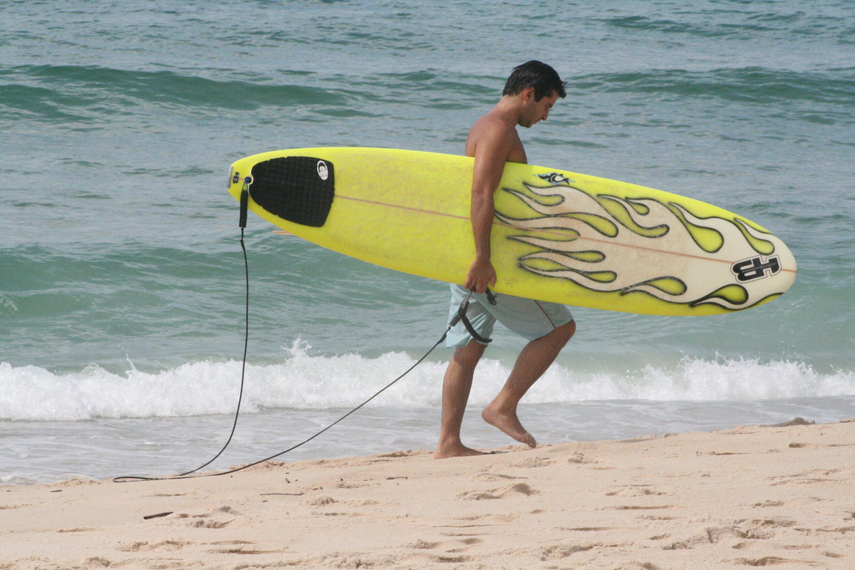 Surfista caminando por la playa con una tabla equipada con leash