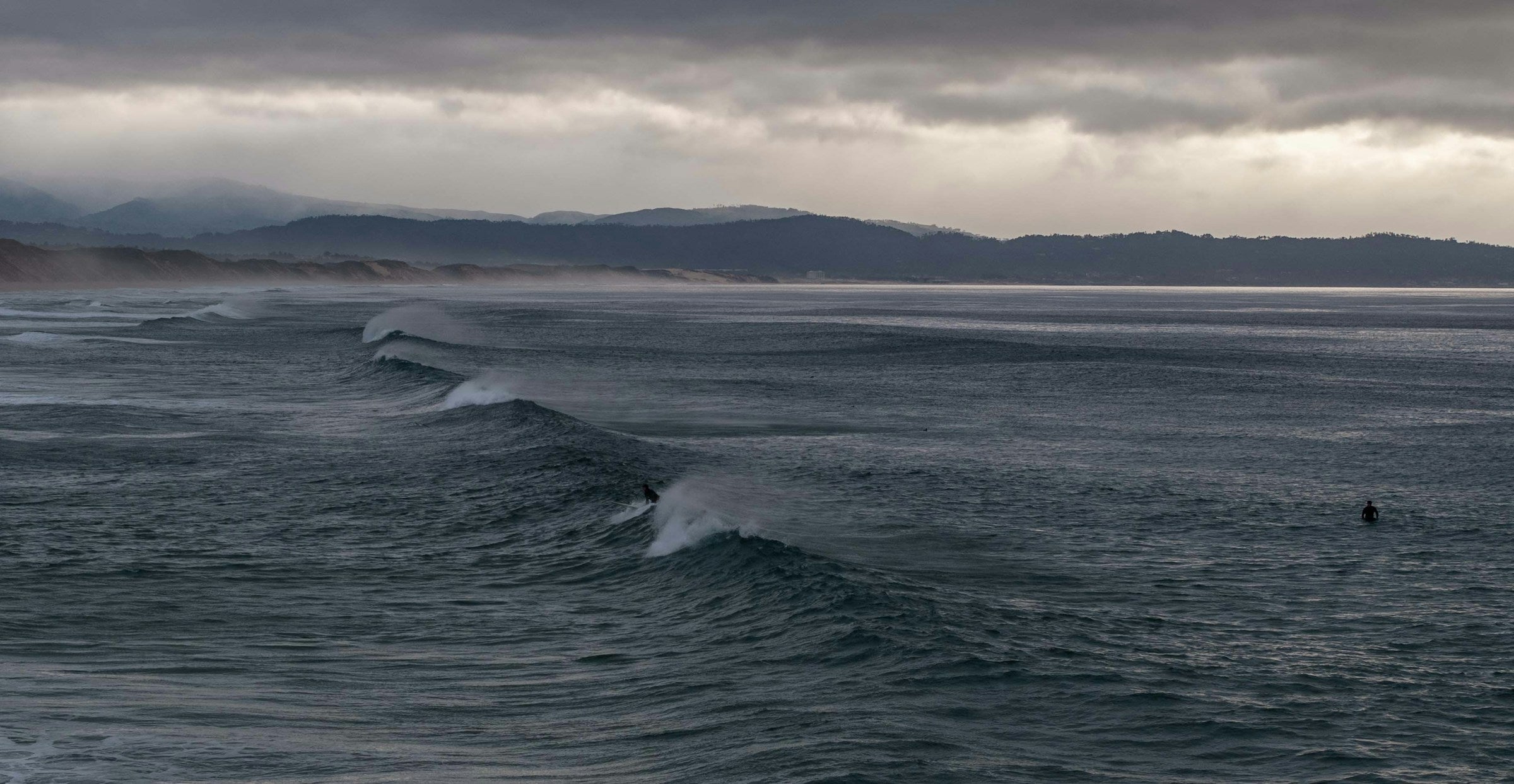 Surfista frente a olas bajo un cielo cubierto