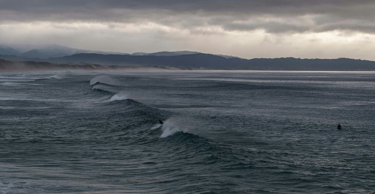 Surfista frente a olas bajo un cielo cubierto