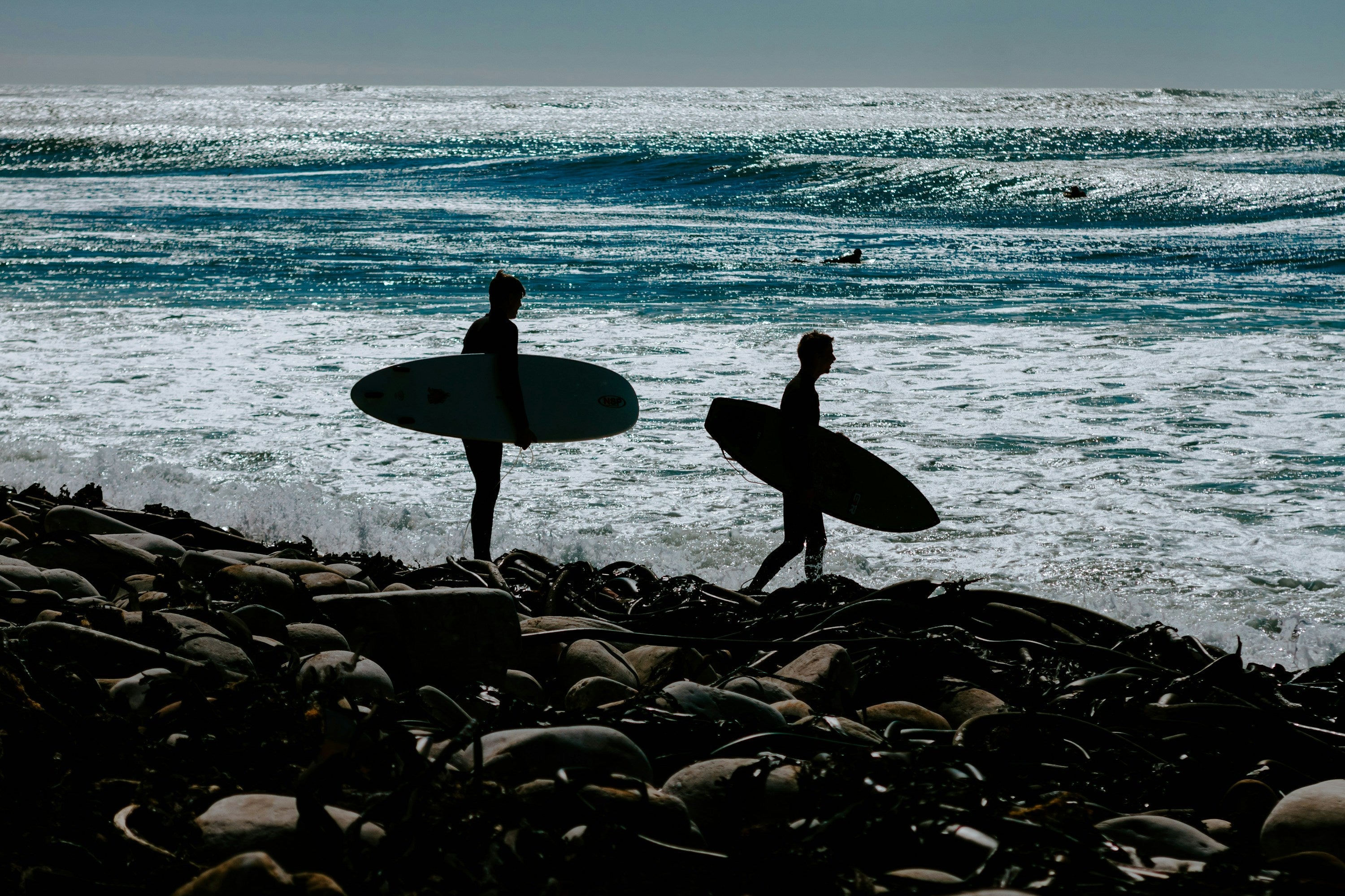 Dos surfistas caminando por una costa rocosa con sus tablas