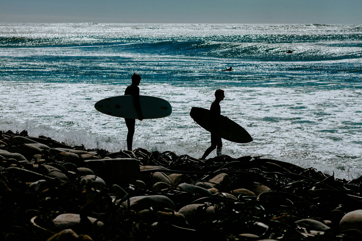 Dos surfistas caminando por una costa rocosa con sus tablas