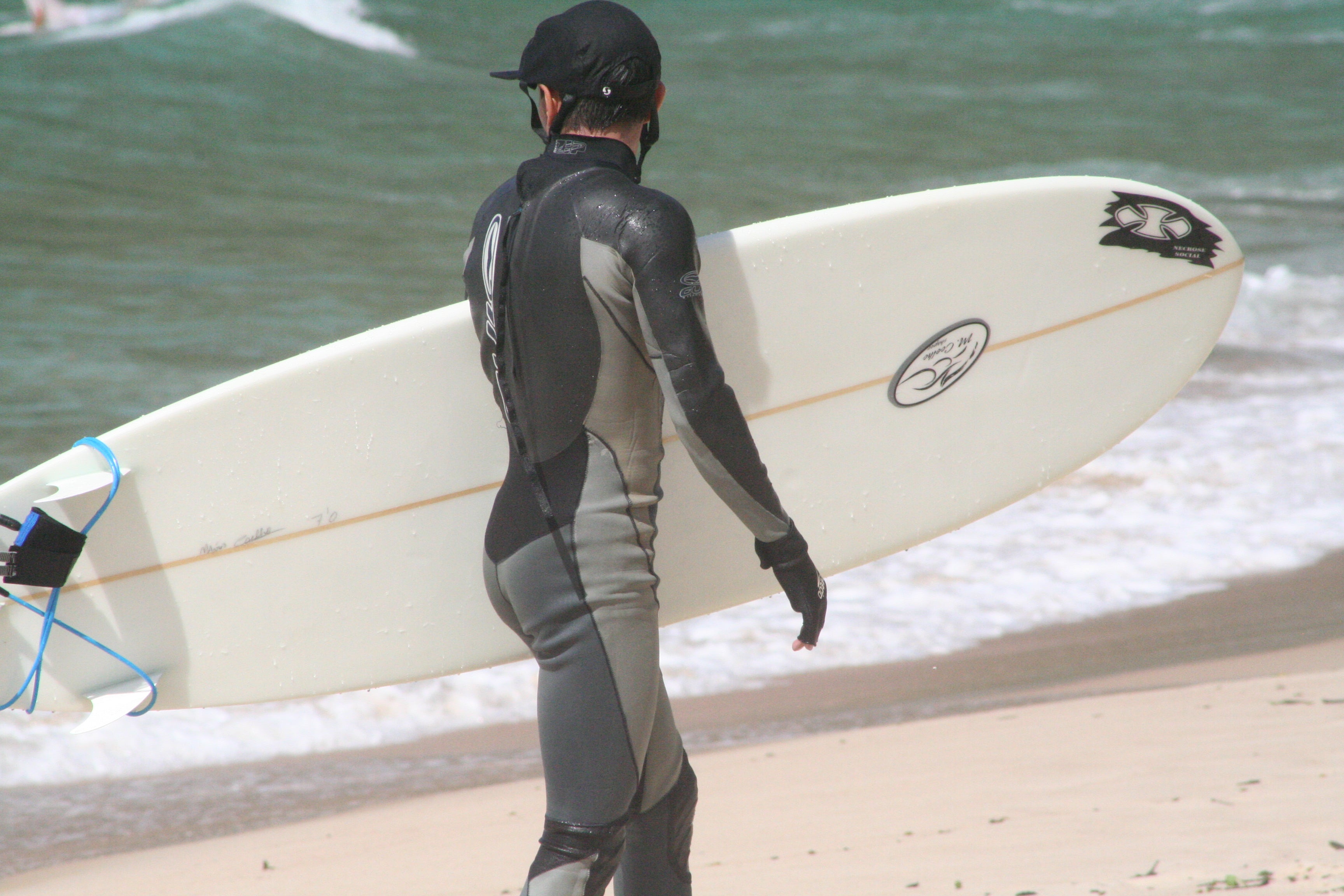 Surfista caminando hacia el mar con tabla y neopreno antes de una sesión; imagen real usada en THE SURF TOWN JOURNAL. Foto: Johntex / Wikimedia Commons, CC BY 2.5.