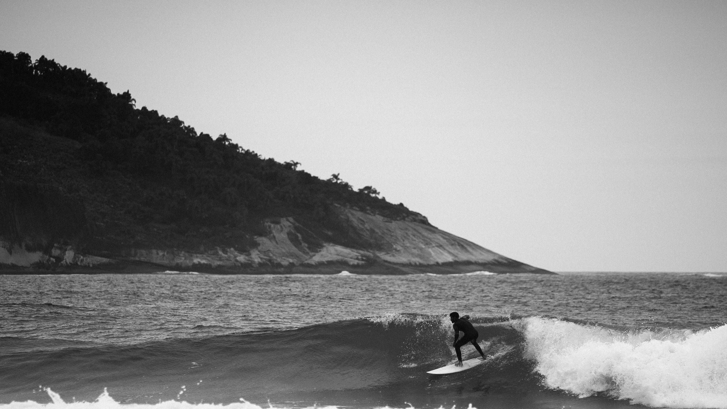 Surfista sobre una ola visto desde la costa en una imagen en blanco y negro