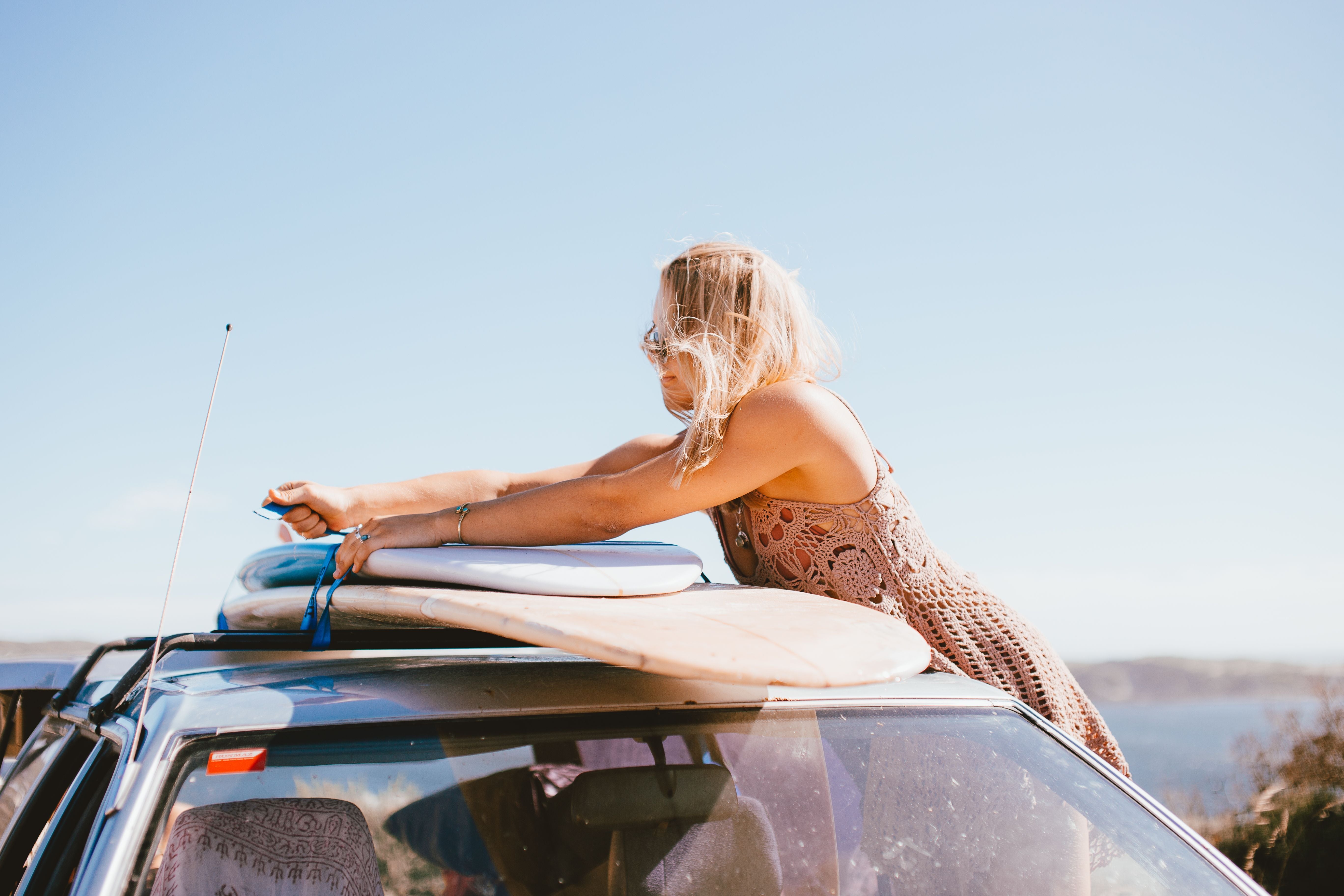 Surfista asegurando tablas de surf sobre la baca de un coche junto al mar
