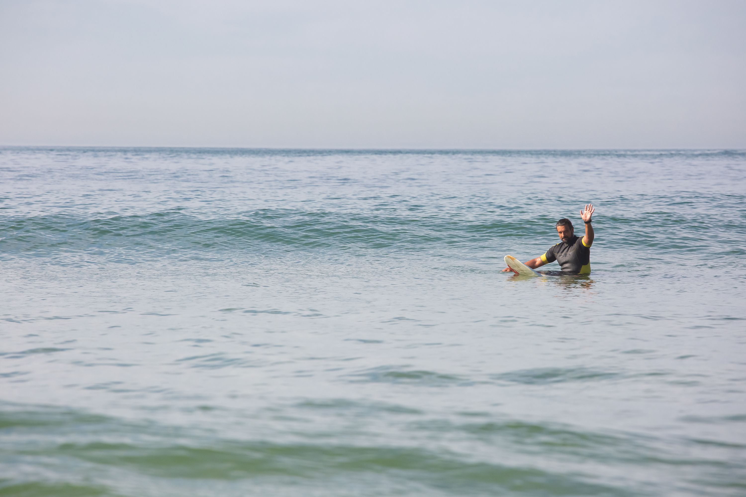 Surfista solo sobre su tabla levantando una mano en el agua