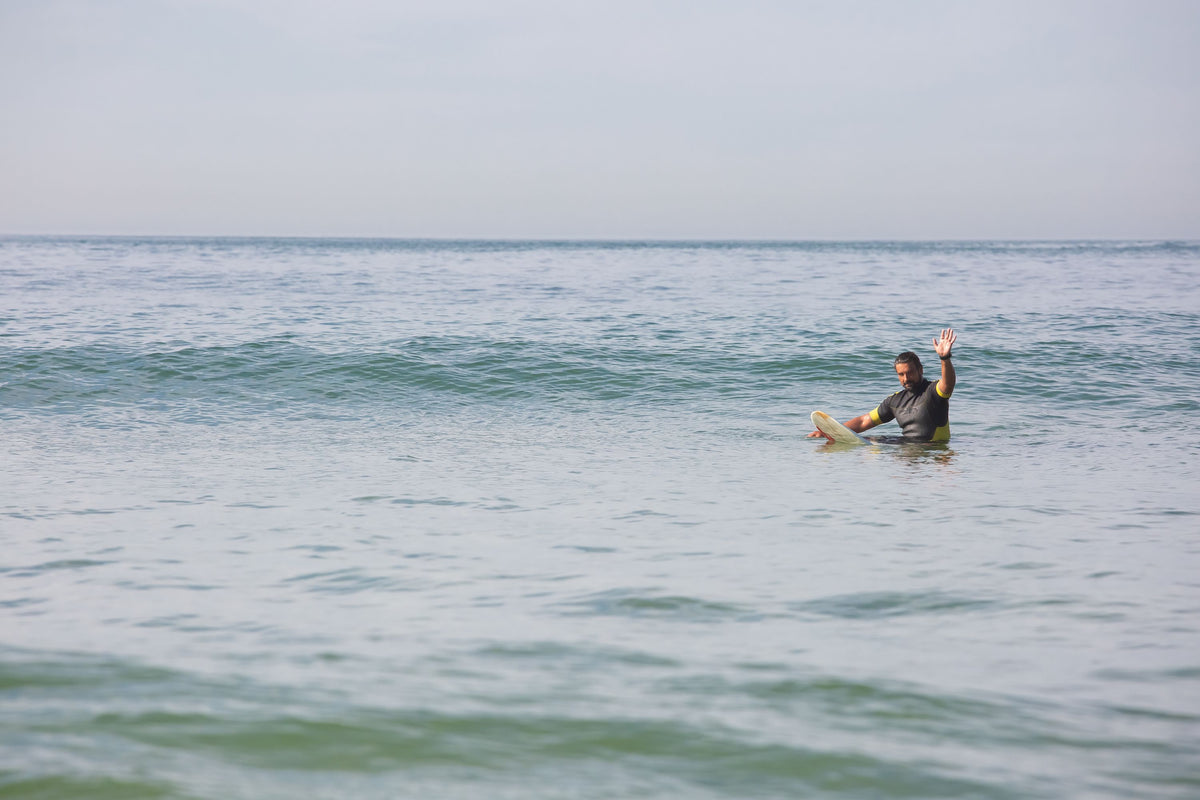 Surfista solo sobre su tabla levantando una mano en el agua