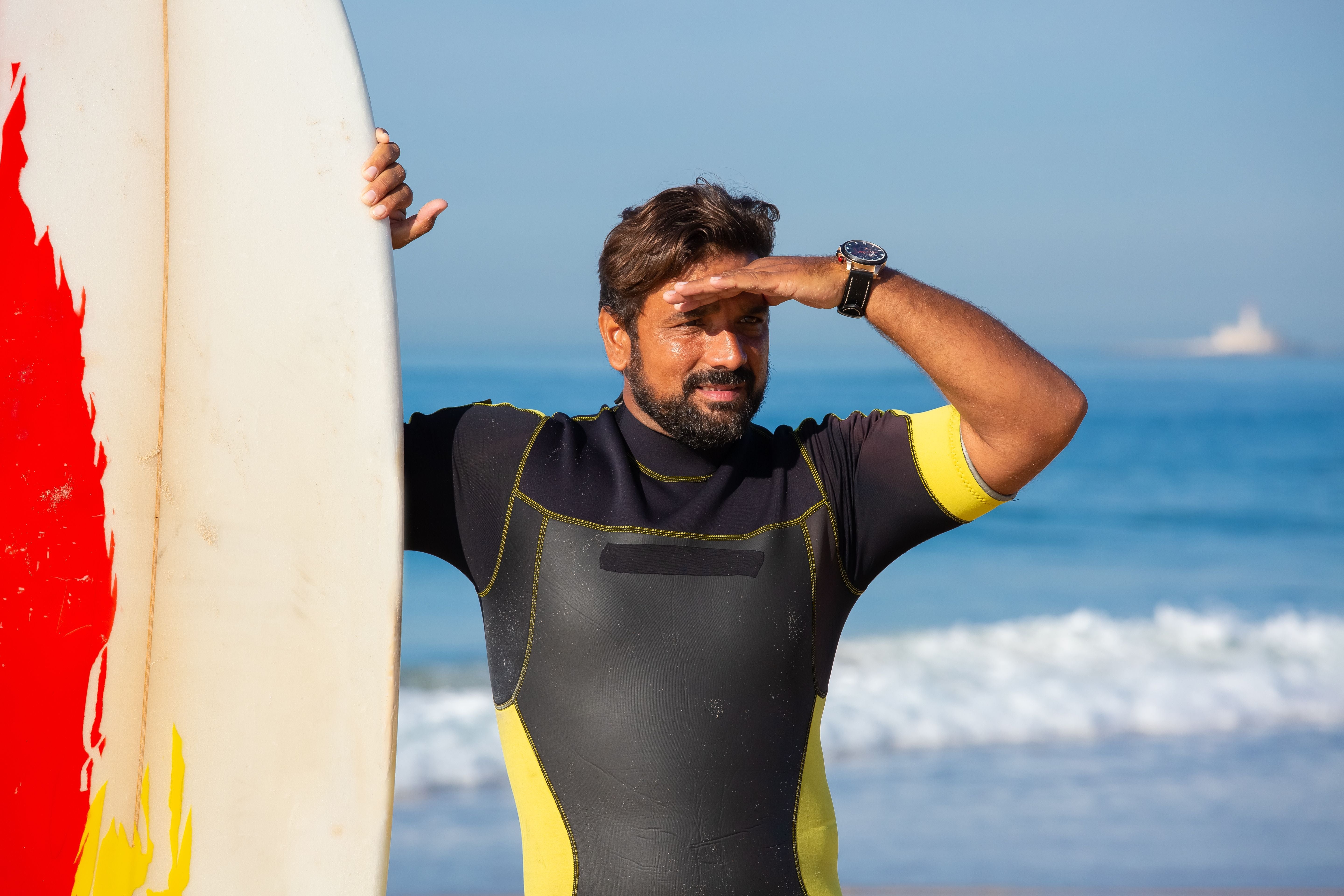 Surfista protegiéndose del sol junto a su tabla en la costa de Portugal