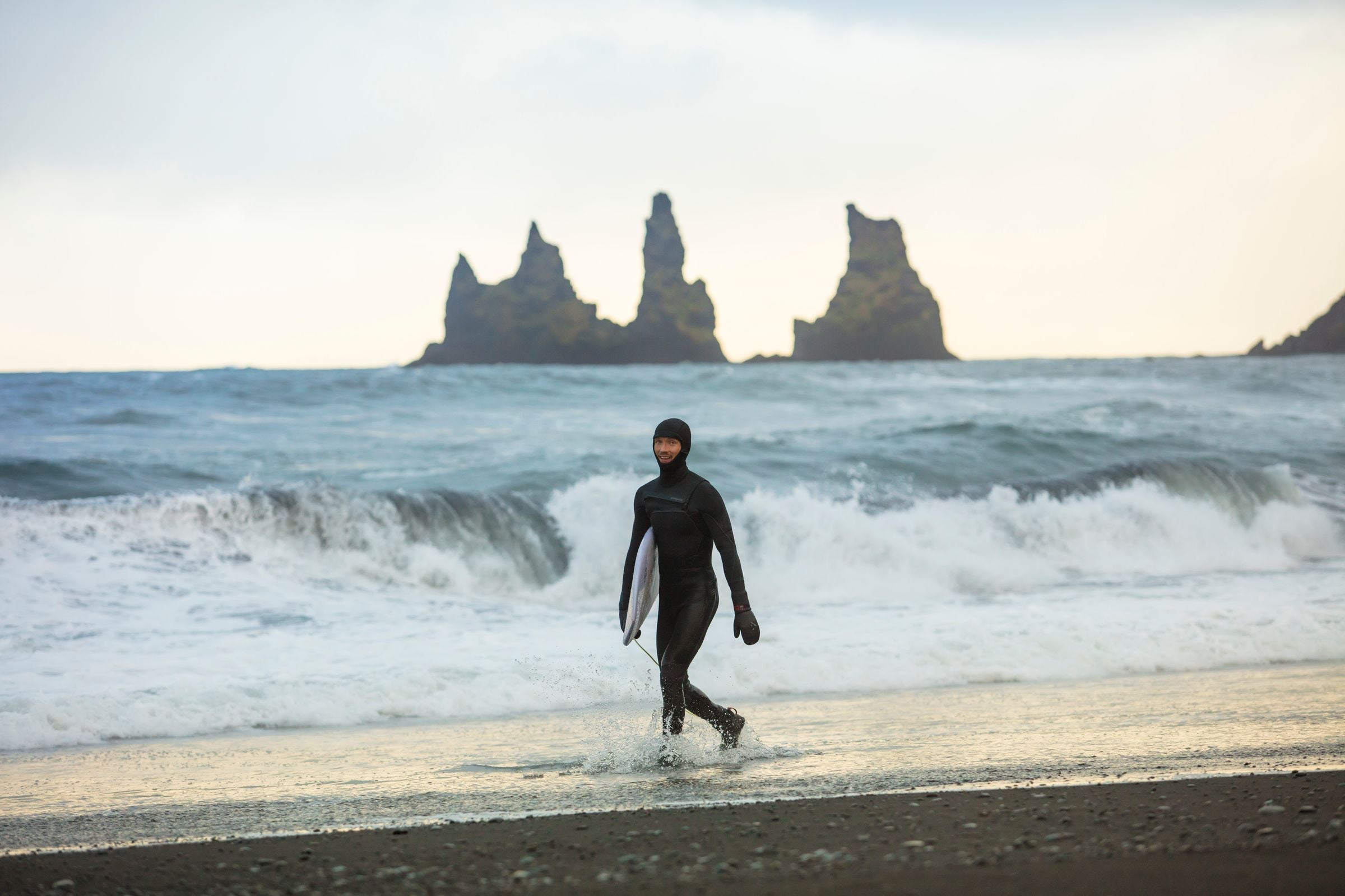 Surfista caminando con su tabla sobre una playa de arena negra