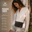 Bolso Roxy Paradise Finder Anthracite mujer en campaña lifestyle premium junto a beach house y atardecer tropical