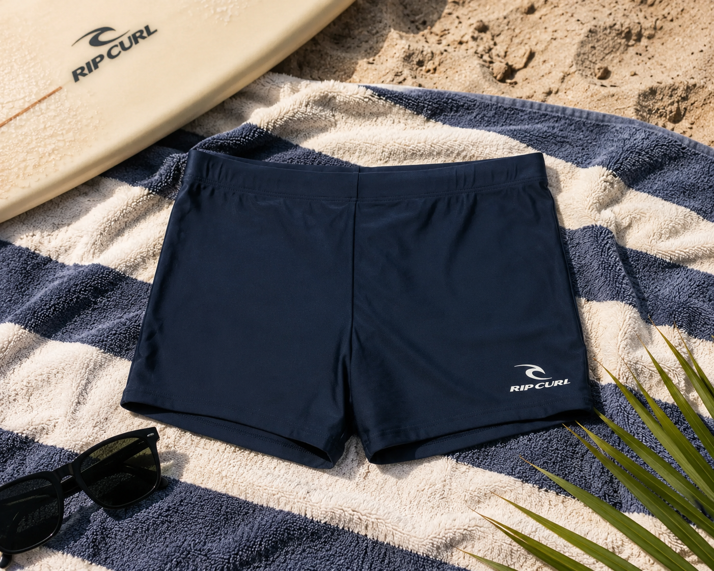 Bañador de natación Rip Curl Corp Boyleg Sluggo Dark Navy sobre toalla de playa en escena surf lifestyle premium