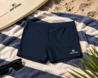 Bañador de natación Rip Curl Corp Boyleg Sluggo Dark Navy sobre toalla de playa en escena surf lifestyle premium